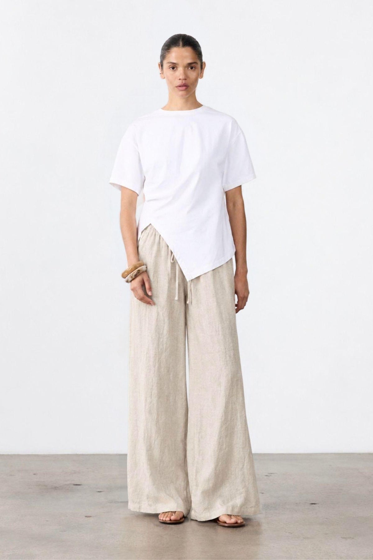 Ruched Jersey Tee by Little Lies — full-length view of a white short-sleeve jersey tee with ruched side detailing and a draped hem, styled with cream wide-leg trousers, available in Australia at Kat and Ko Clothing.