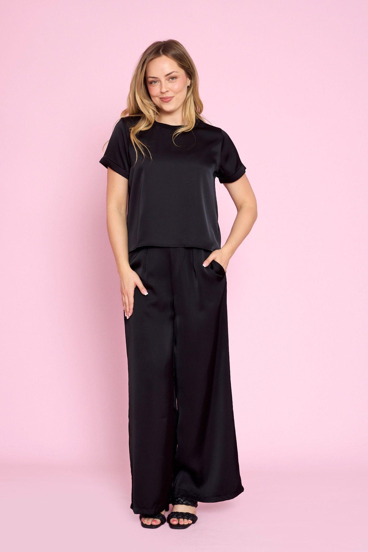 Fria The Label Greta Satin Tee in Black full-length view styled with black wide leg pants