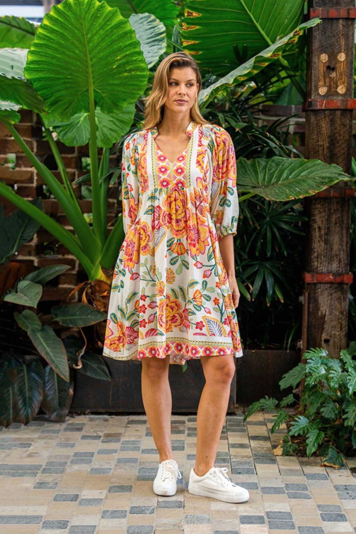 Marwa Dress by Boho Australia — full-length front view of the colourful spliced-print dress with band collar, V-neckline and billowing three-quarter sleeves, styled with white sneakers in a tropical garden, available in Australia at Kat and Ko Clothing