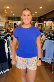 Little Lies Rhodes Tee in Cobalt front view showing the round neck and cuffed sleeves, with floral shorts