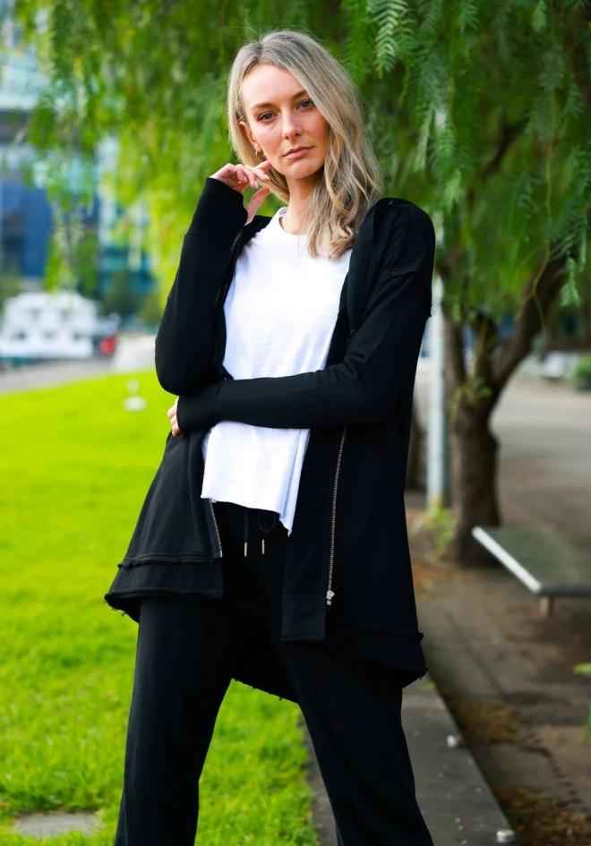 Charlie Jacket in Black by 3rd Story The Label — outdoor lifestyle shot of longline black hooded cardigan jacket with side zip and raw-edge hi-lo hem, styled with a white tee and black wide-leg pants, available in Australia at Kat and Ko Clothing