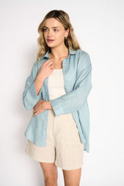 Boyfriend Shirt in Aqua Haze by Little Lies — three-quarter front view of relaxed aqua haze linen-blend shirt worn open over a white tank, styled with beige linen shorts, shop in Australia at Kat and Ko Clothing