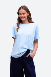 Label of Love Easy Tuck Tee in Light Blue, front view with the hem tucked, worn with navy pants