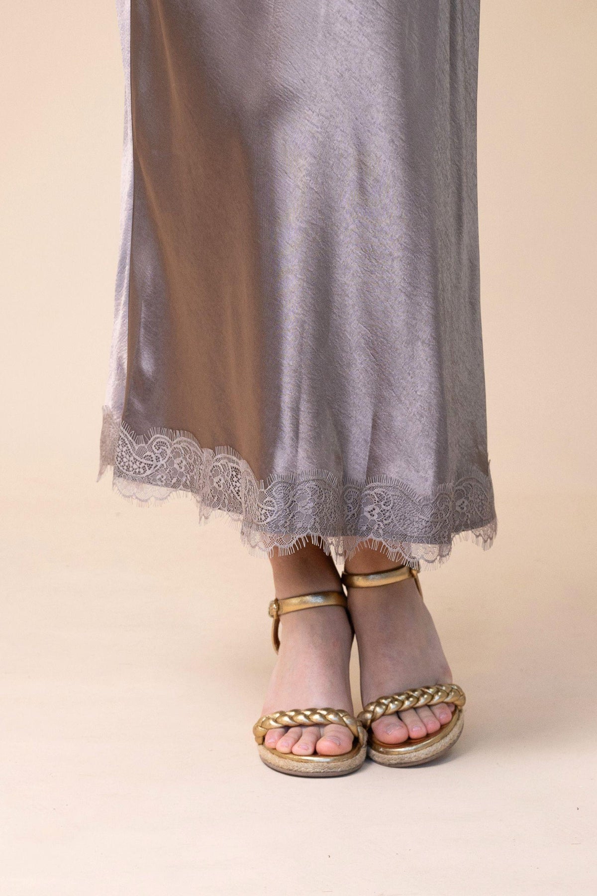 Fria The Label Bardot Satin Midi Skirt in Taupe close-up of the lace trim hem with gold sandals
