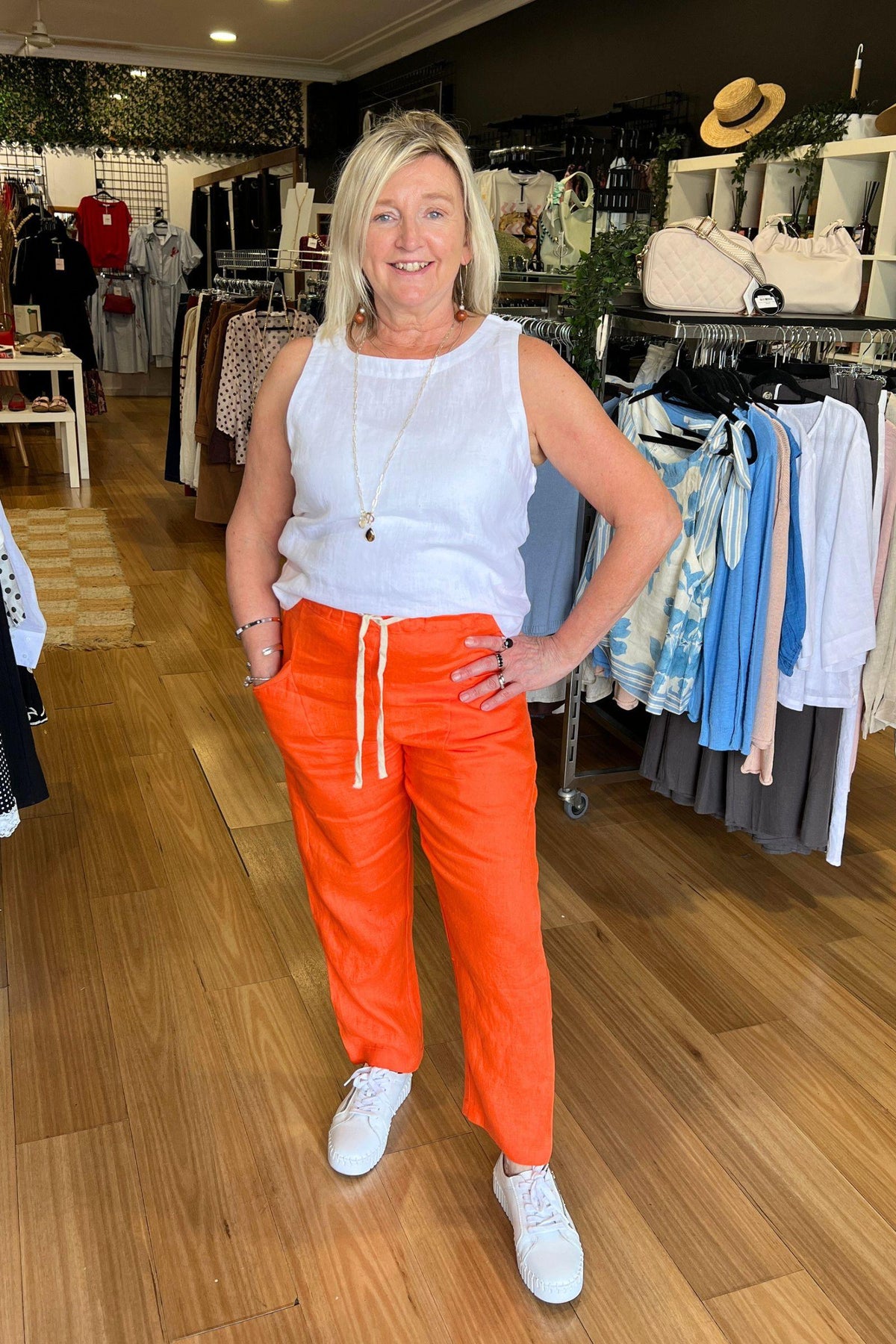 Little Lies Luxe Pants in Vivid Orange full-length front view with a white tank and white sneakers