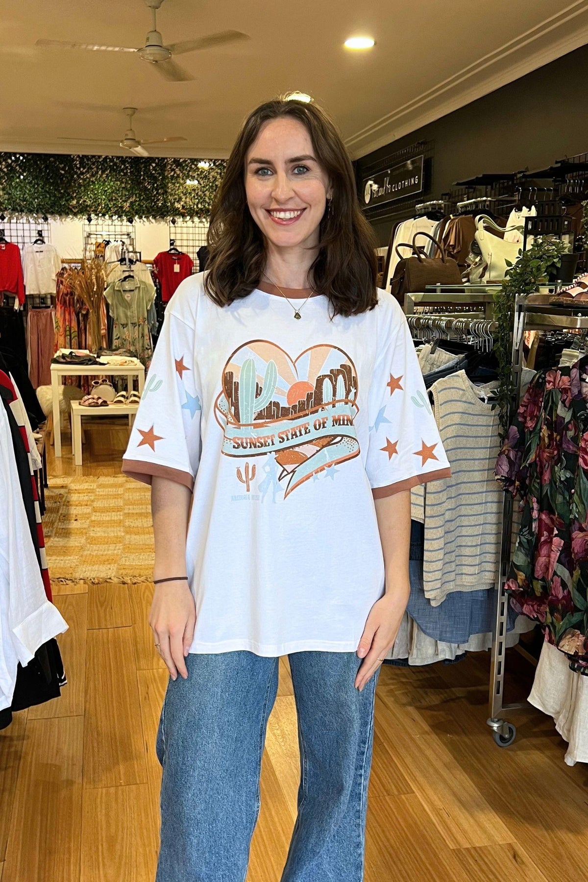 Sunset State of Mind Tee - White by Coco Cartel, front view of the oversized white graphic tee with printed sleeves, styled with blue jeans in Australia at Kat and Ko Clothing