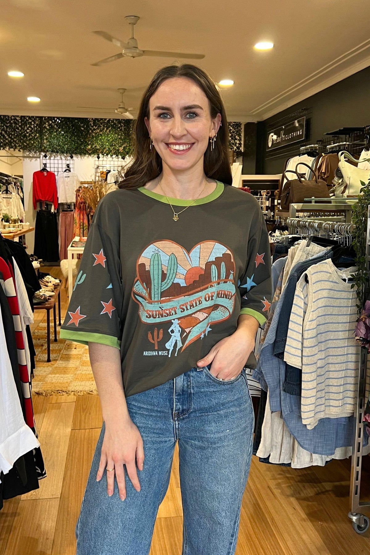 Sunset State of Mind Tee - Charcoal by Coco Cartel, front view of the oversized charcoal graphic tee with printed sleeves, styled with blue jeans in Australia at Kat and Ko Clothing