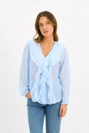 Claire Linen Blouse in Ice Blue by Worthier — front view of the ruffled V-neckline linen blouse with long sleeves, styled with blue denim jeans, available in Australia at Kat and Ko Clothing