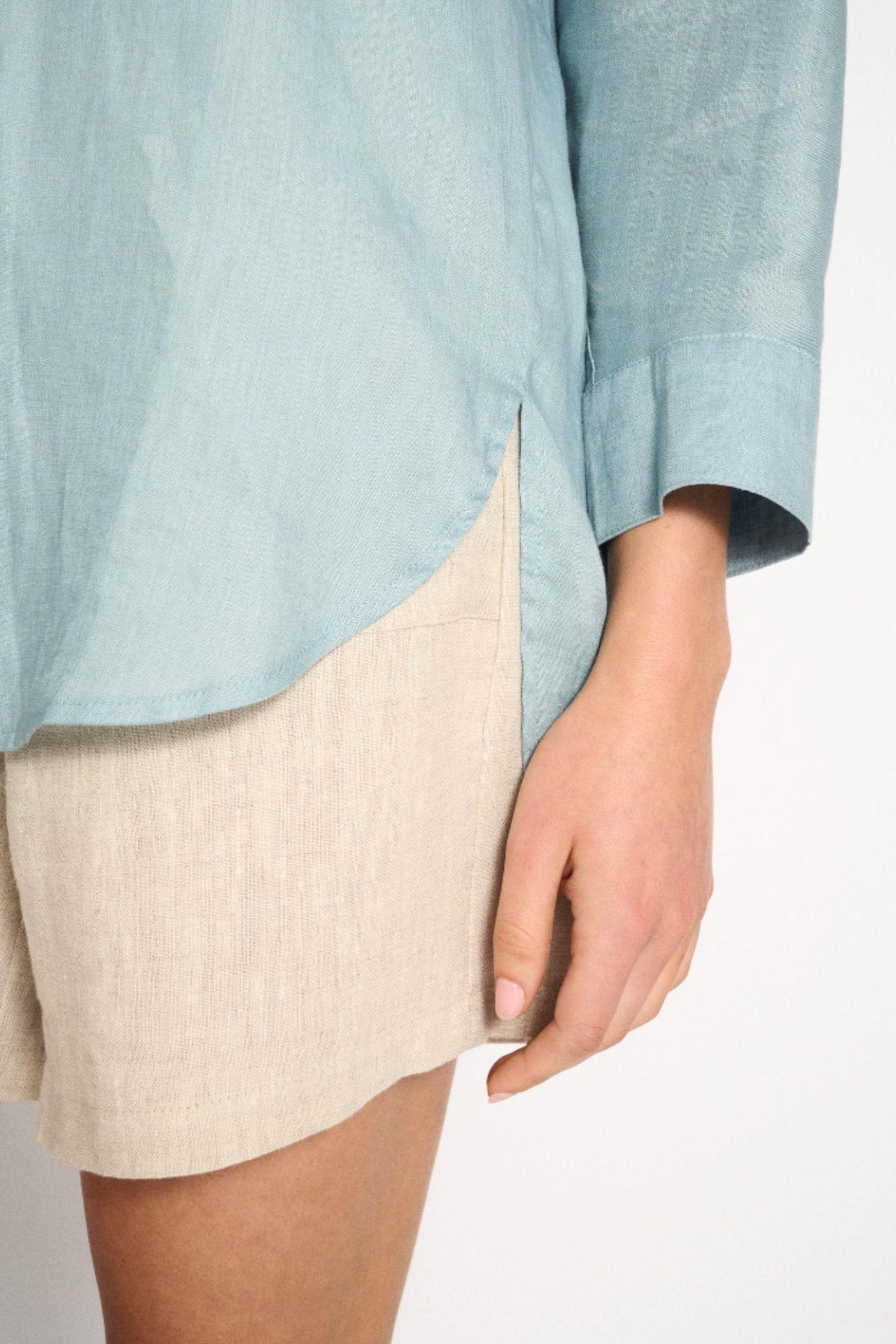 Little Lies Boyfriend Shirt in Aqua Haze — close-up of the curved relaxed hem and three-quarter sleeve cuff of the aqua haze linen-blend shirt, styled with beige linen shorts, available in Australia at Kat and Ko Clothing