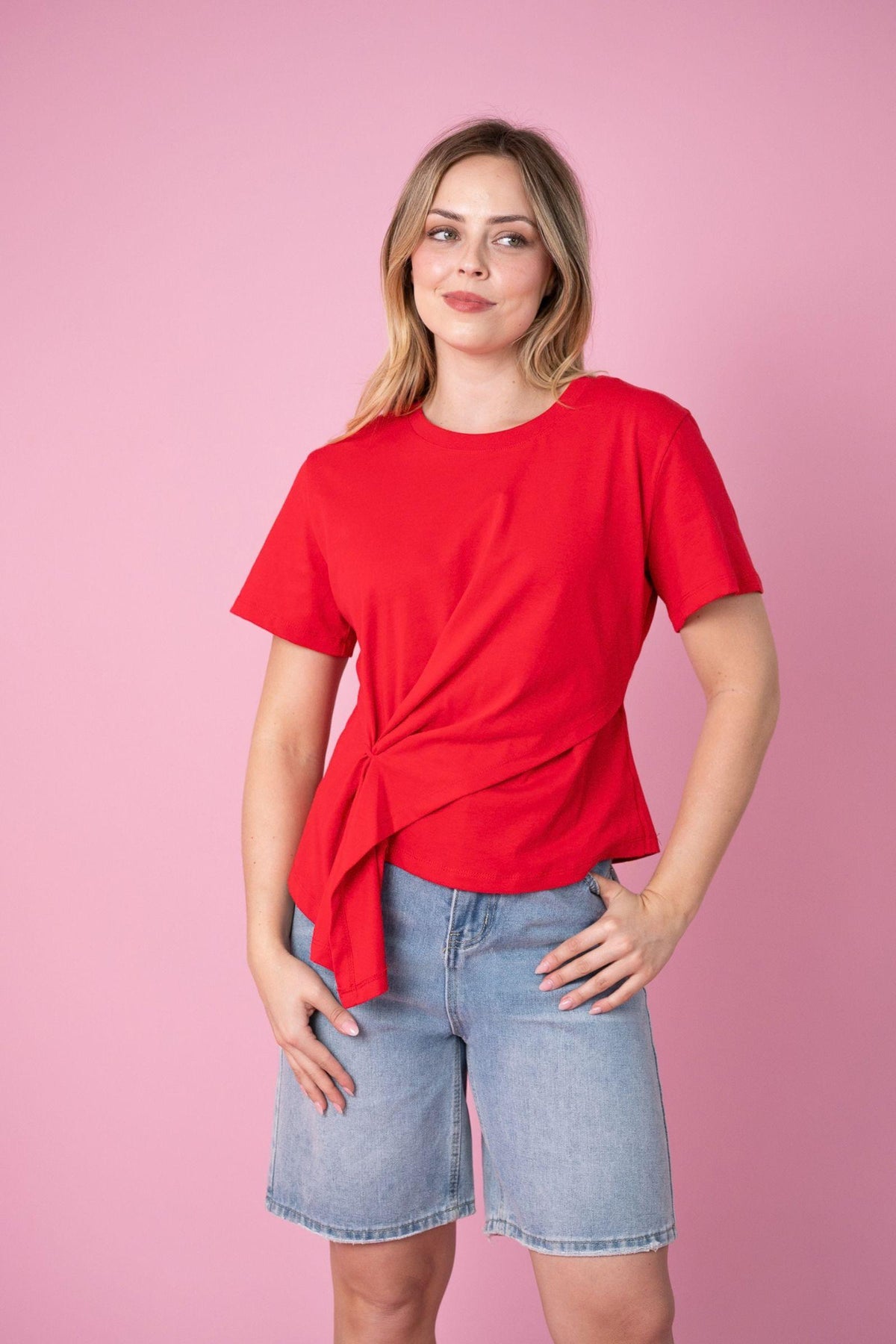 Fria The Label Ellery Tee in Red, angled front view with hand on hip and denim shorts