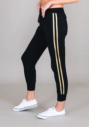 Gabby Stripe Jogger in Black by 3rd Story The Label — side profile showing twin gold metallic stripes on black tapered cotton jersey jogger with ribbed ankle cuffs, styled with white sneakers, available in Australia at Kat and Ko Clothing