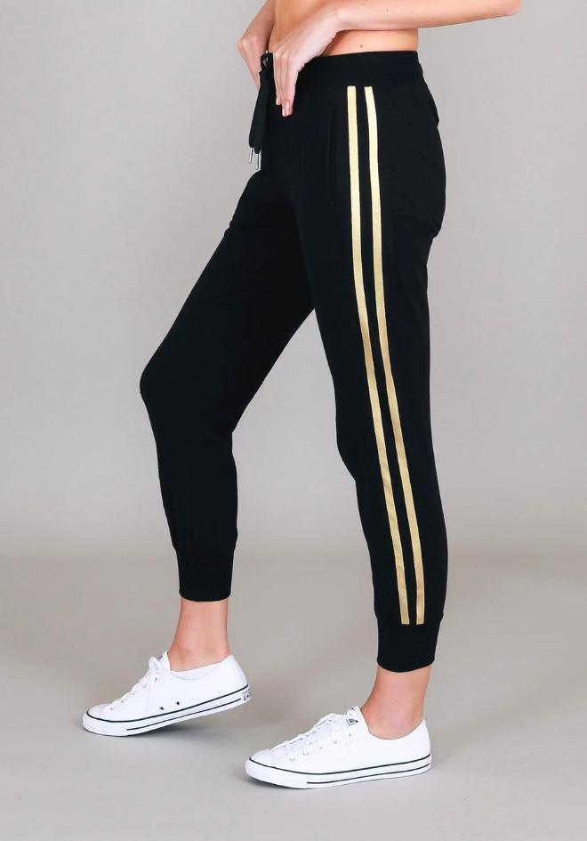 Gabby Stripe Jogger in Black by 3rd Story The Label — side profile showing twin gold metallic stripes on black tapered cotton jersey jogger with ribbed ankle cuffs, styled with white sneakers, available in Australia at Kat and Ko Clothing
