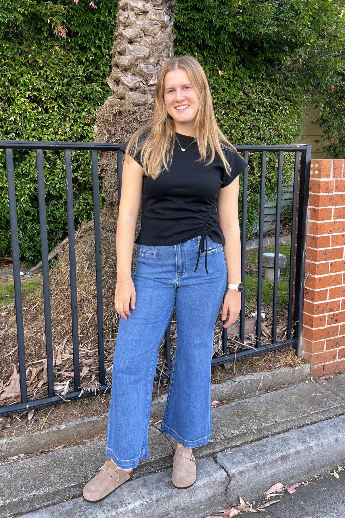 Derby Jeans Light Denim Wakee Jeans — full-length lifestyle front view of wide-leg light wash denim with contrast stitched hem, styled with a black ruched cap sleeve tee and tan suede mules, shop in Australia at Kat and Ko Clothing