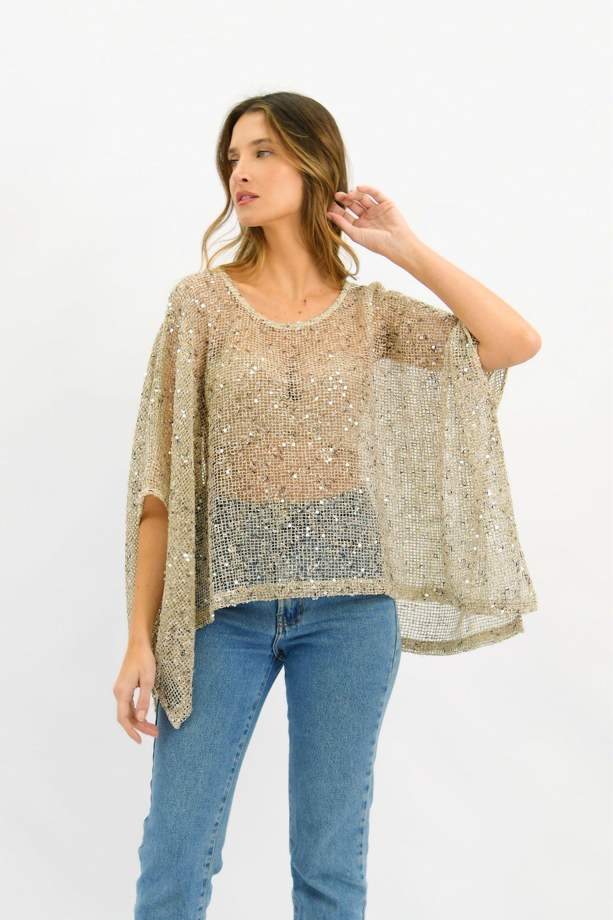 Golden Hour Sequin Top in Beige by Worthier — angled front view of oversized sheer sequin poncho in champagne beige with batwing sleeves and scoop neckline, styled with blue denim jeans, shop in Australia at Kat and Ko Clothing