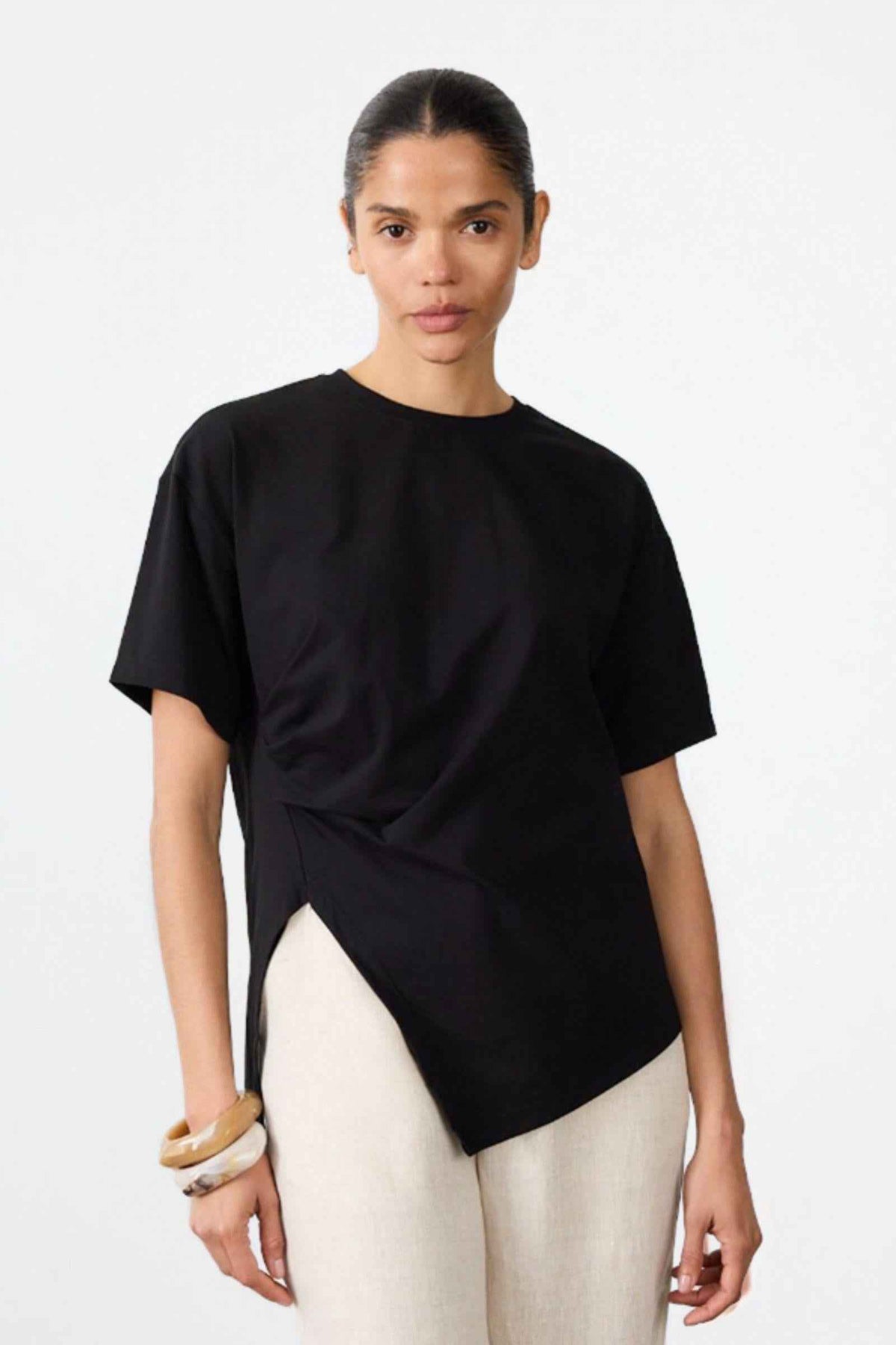 Little Lies Ruched Jersey Tee in Black, front view of the draped ruched hem styled with cream pants