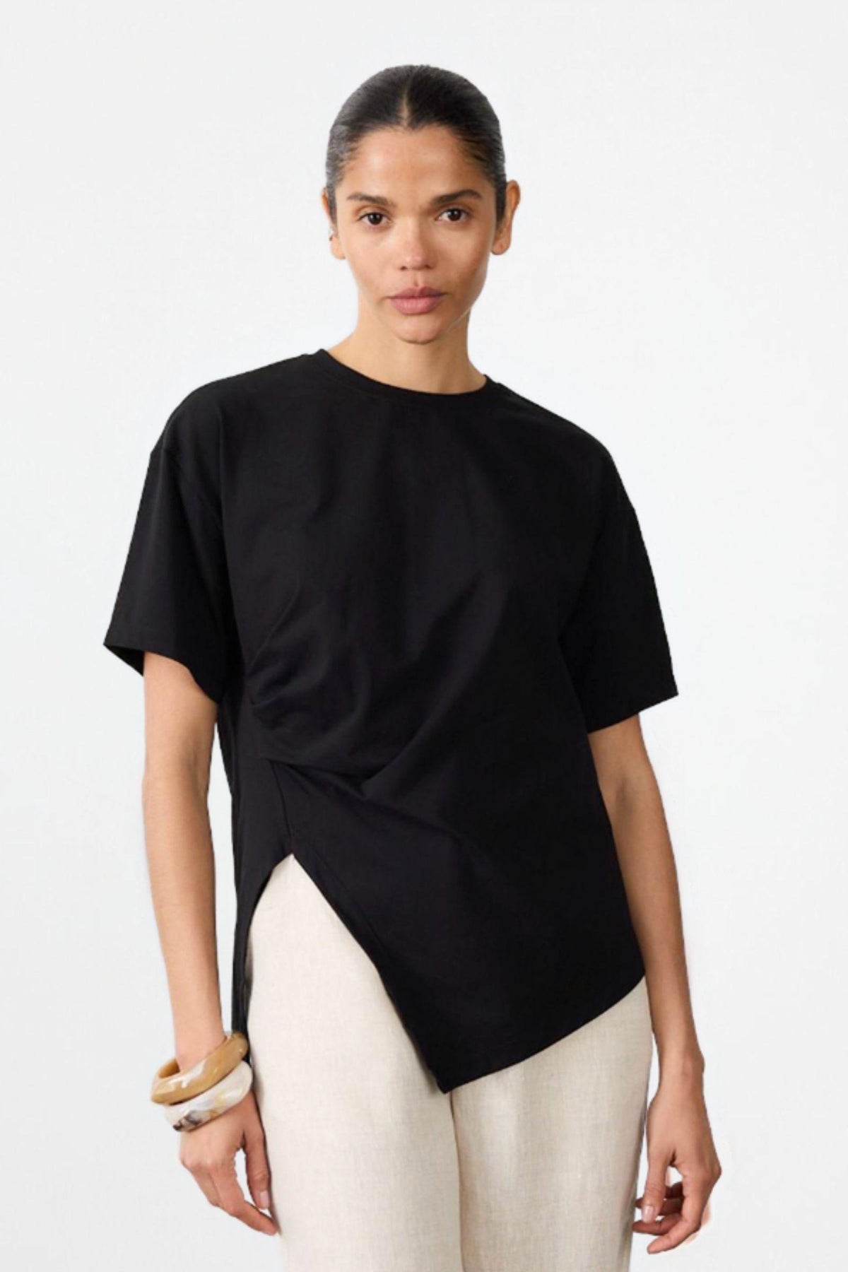 Ruched Jersey Tee by Little Lies — front view of a black short-sleeve jersey tee with ruched side detailing and a draped hem, styled with cream trousers, available in Australia at Kat and Ko Clothing.