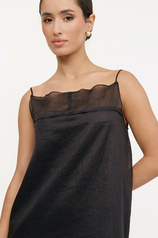 A model wearing a black, sleeveless, square neckline, thin straps, and side splits river dress.
