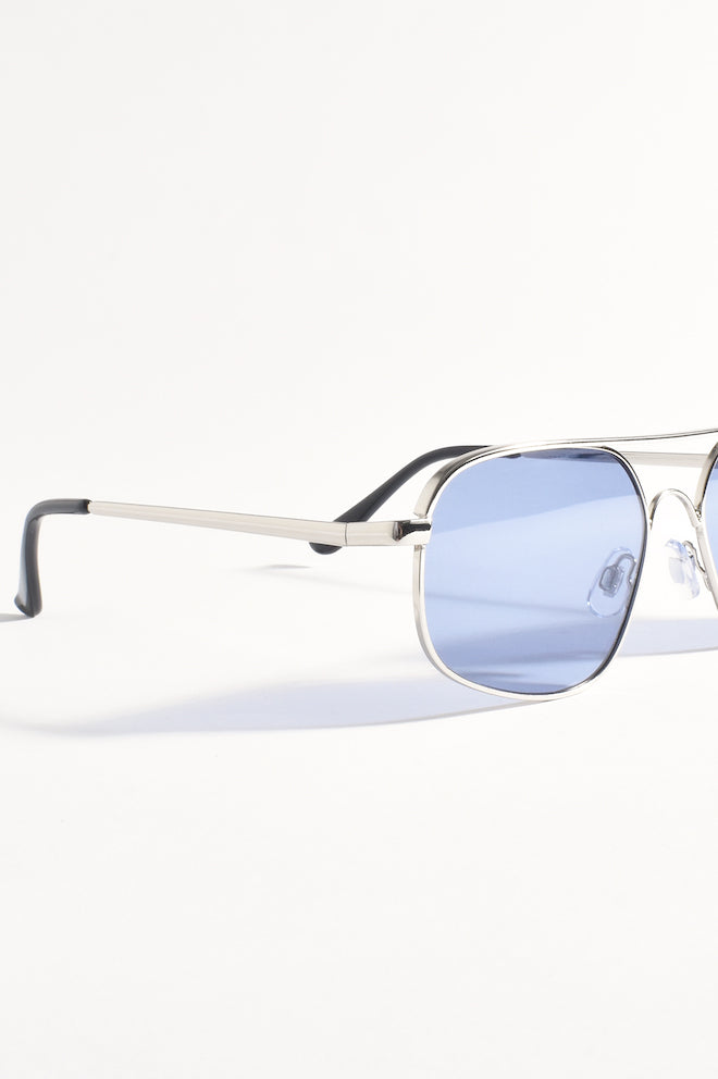 Aviator-style sunglasses with silver frames and blue lenses placed on a white surface.