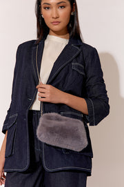 A woman wearing a white top and a charcoal gray shearling pouch cross body bag with a denim jacket and trousers.
