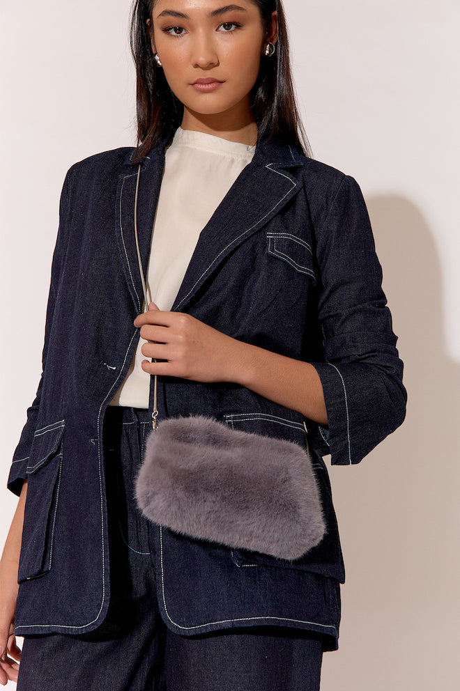 A woman wearing a white top and a charcoal gray shearling pouch cross body bag with a denim jacket and trousers.
