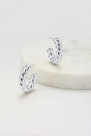 A pair of silver-colored hoop earrings displayed on a marble surface.