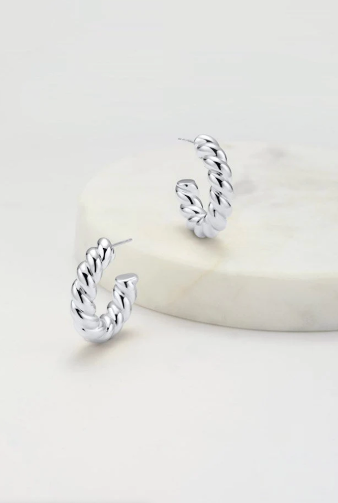 A pair of silver-colored hoop earrings displayed on a marble surface.