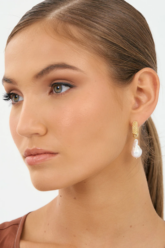 Close-up of a woman wearing gold earrings with white pearls on a neutral background