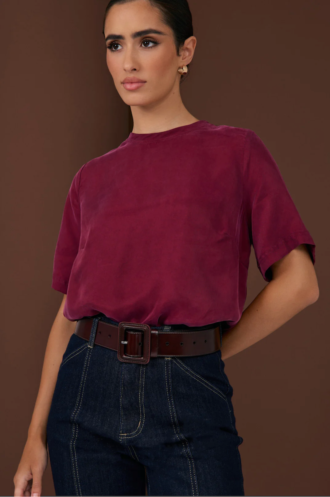 Woman wearing a burgundy t-shirt and dark jeans against a brown background
