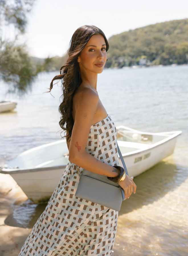 Woman in a patterned dress standing by a lake with a boat in the background