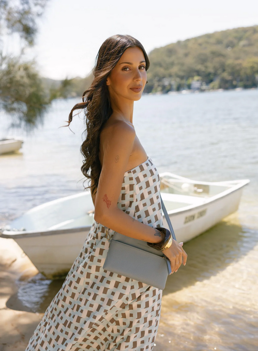 Woman in a patterned dress standing by a lake with a boat in the background
