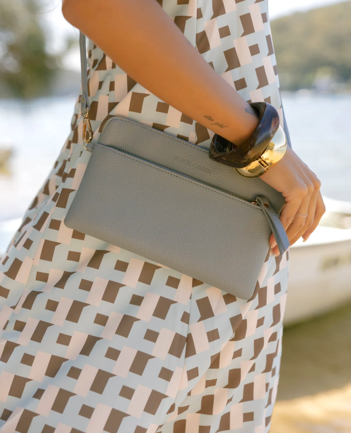 Person holding a gray clutch with a patterned dress and watch, blurred natural background