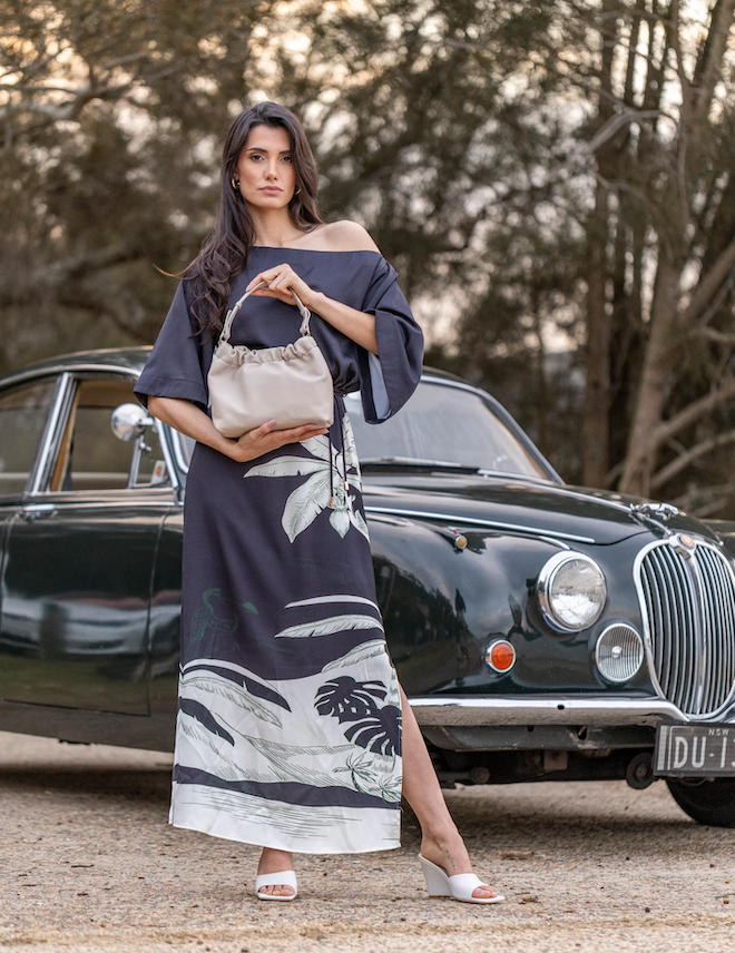 Woman in a long dress holding a handbag in front of a vintage car