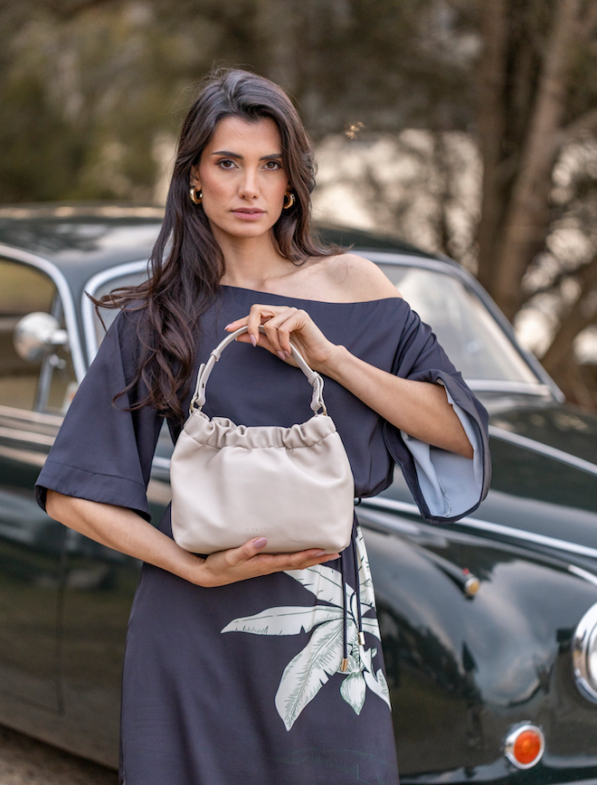 Woman holding a beige handbag in front of a vintage car