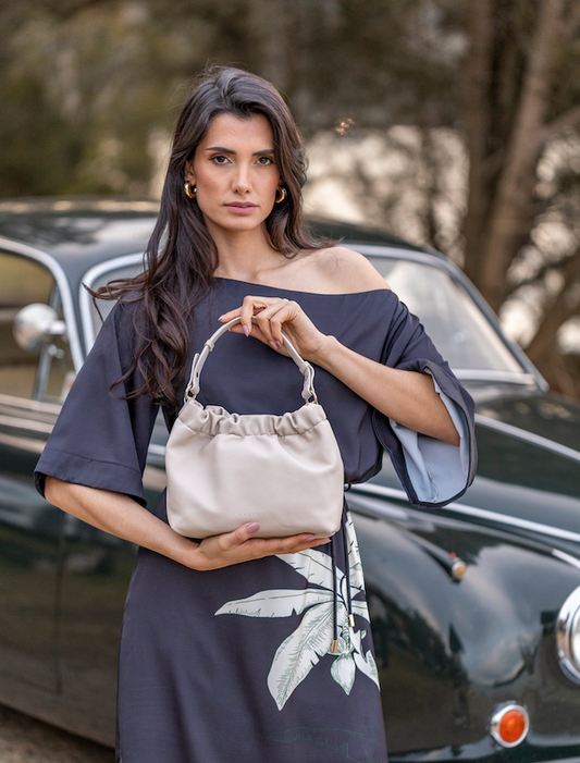 Woman holding a beige handbag in front of a vintage car