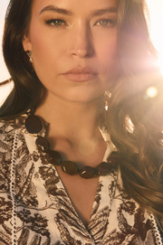 Woman wearing a patterned top and dark necklace with a blurred background