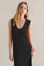 A woman wearing a black knit dress with a scoop neck and side splits, paired with a statement necklace.