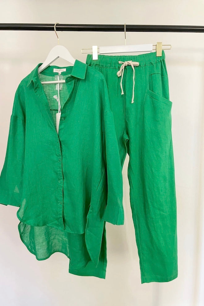 Green linen shirt and pants on hangers against a white background