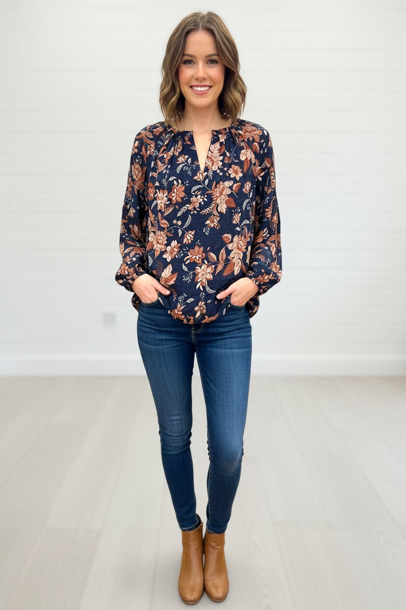A woman wearing a Kat and Ko Clothing Hallie Blouse with a navy blue floral print, long sleeves, and a split neckline.