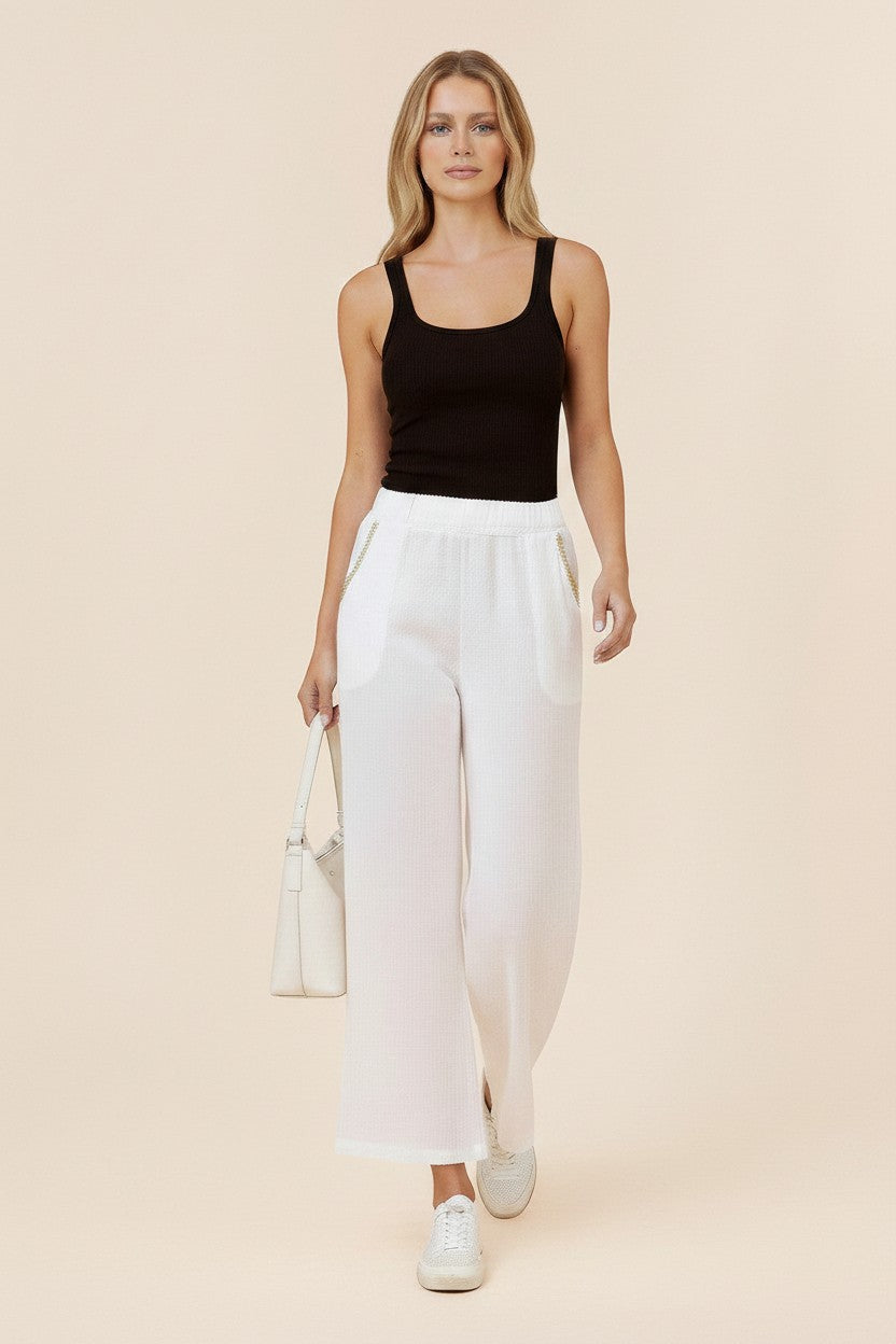 Kat and Ko Clothing white Italian linen straight-leg pants with gold pocket trim worn by a model with a black tank top