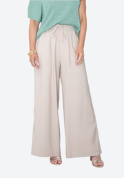 Person wearing light beige wide-leg pants with a green top on a white background