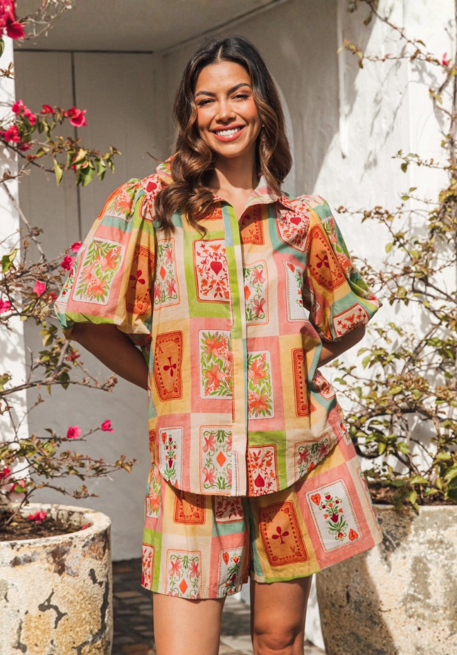 Woman wearing a colorful patchwork outfit standing outdoors with flowers in the background