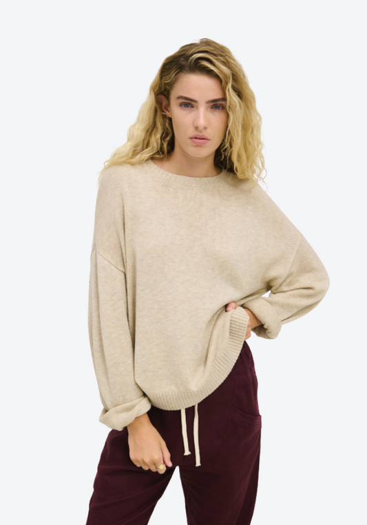 Woman wearing a beige sweater and maroon pants on a white background