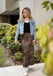 Woman wearing a denim jacket, black top, and leopard print pants standing outdoors.