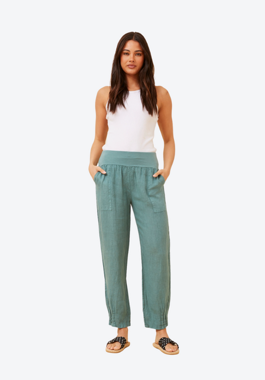 Woman wearing teal pants and a white top on a white background