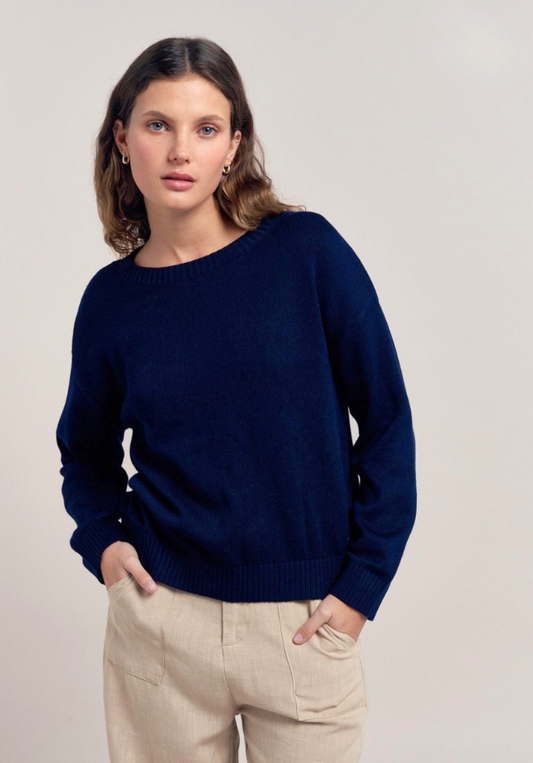 Woman wearing a navy blue sweater and beige pants against a plain background