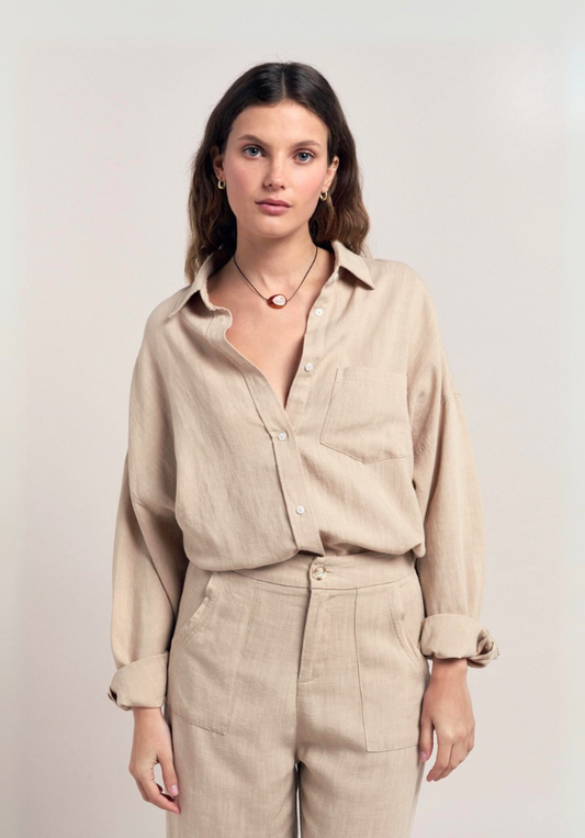 Woman wearing a beige shirt and pants against a plain background
