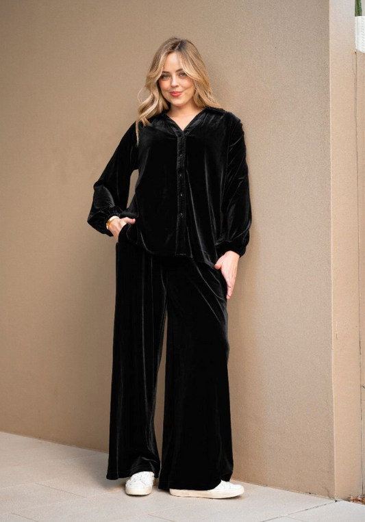 Woman wearing a black velvet outfit against a beige wall.