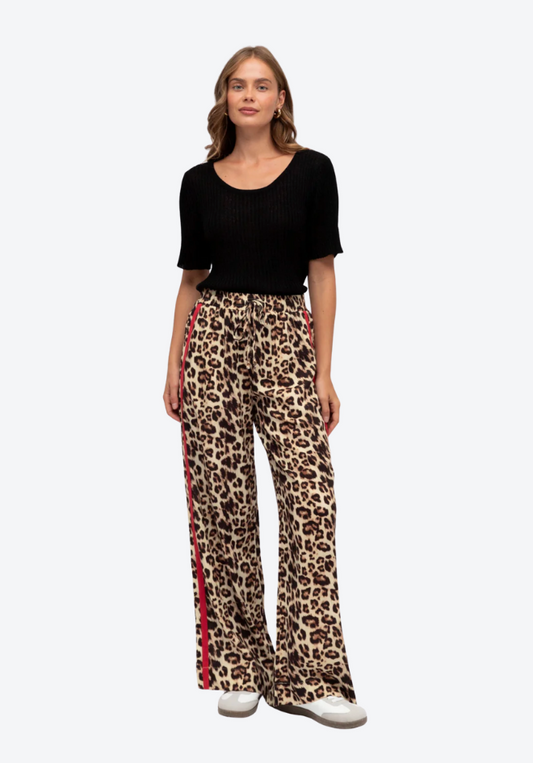Woman wearing a black top and leopard print pants with red stripes on a white background
