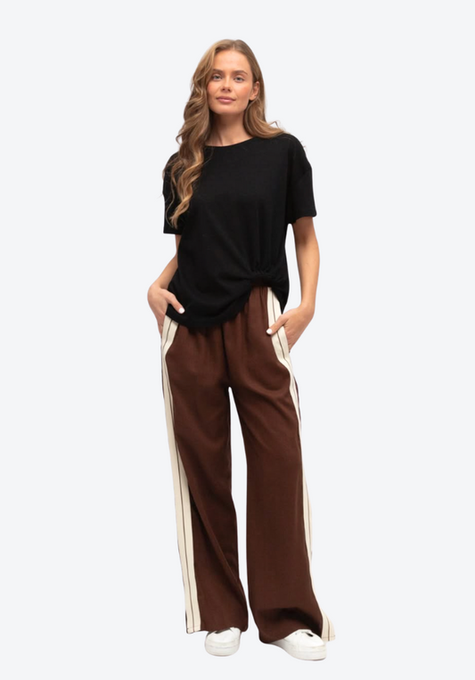 Woman wearing a black top and brown pants with white stripes on a white background