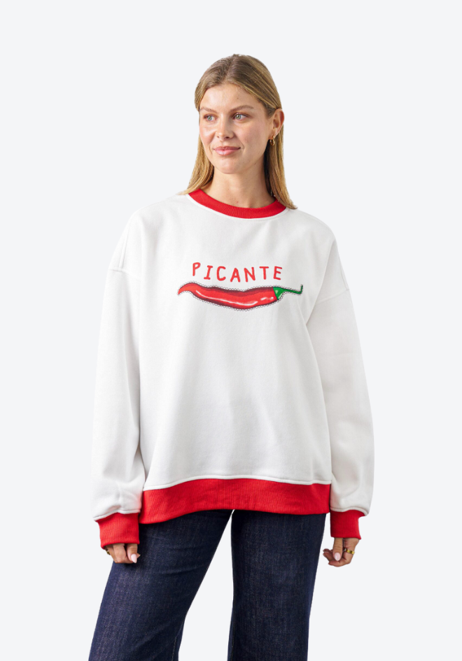 Woman wearing a white sweatshirt with red accents and 'PICANTE' text and pepper graphic on a white background